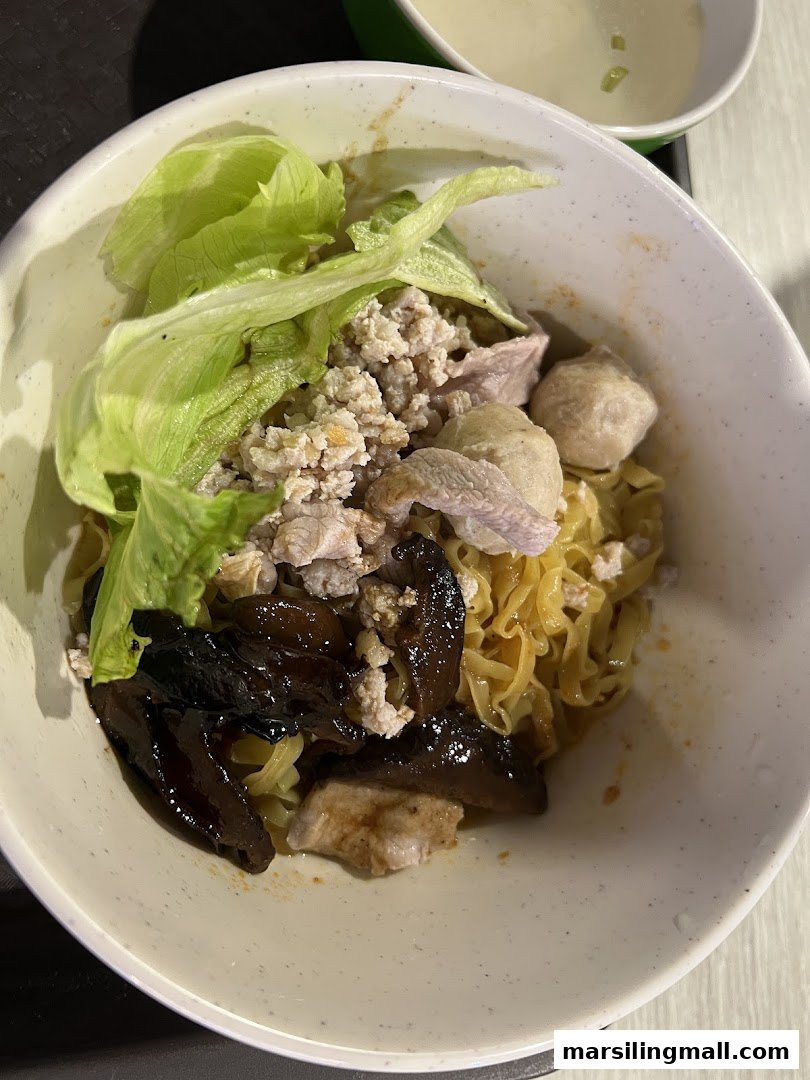 A close-up of a bowl of minced meat noodles with lettuce, mushrooms, and meat slices, served with a side of soup.
