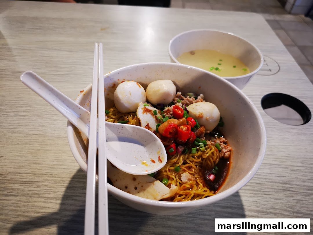 A vibrant bowl of minced meat noodles with fish balls, chili, and a side of clear soup.