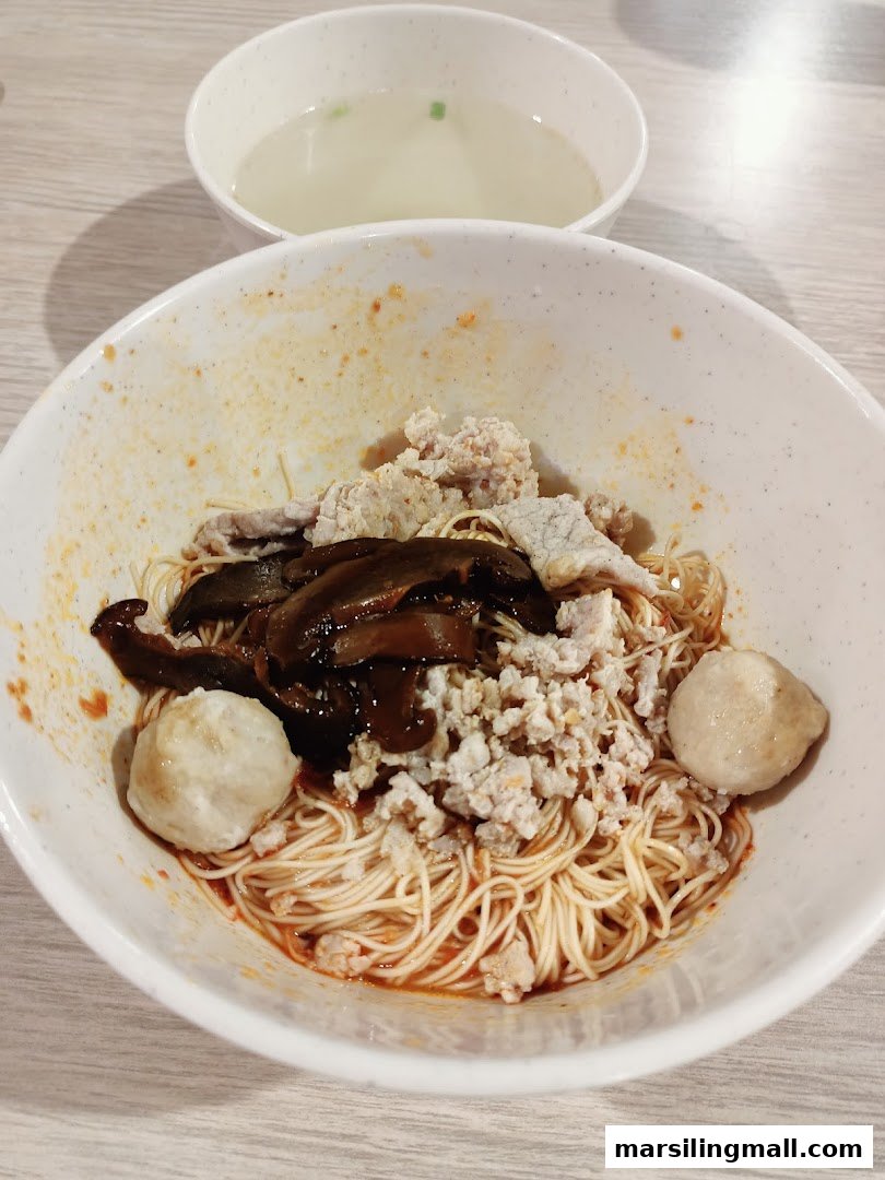 A close-up of a delicious bowl of minced meat noodles with mushrooms and fish balls, served with a side of soup.