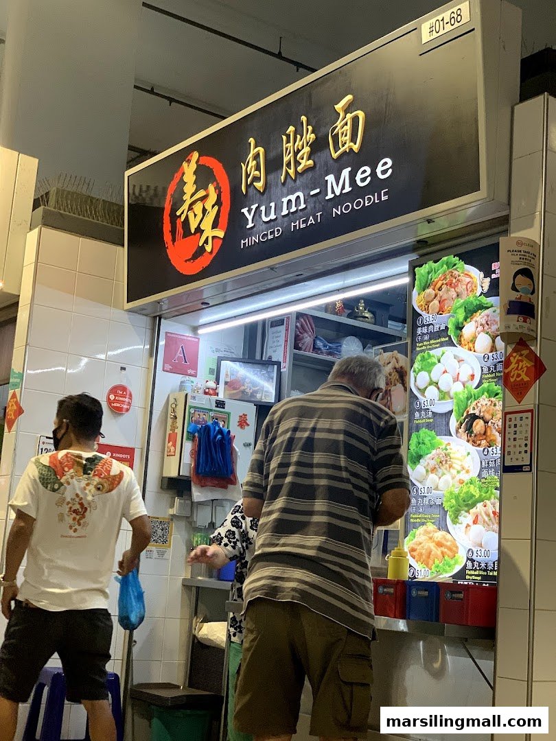 A bustling food stall, Yum-Mee Minced Meat Noodle, with customers ordering from a vibrant menu display.
