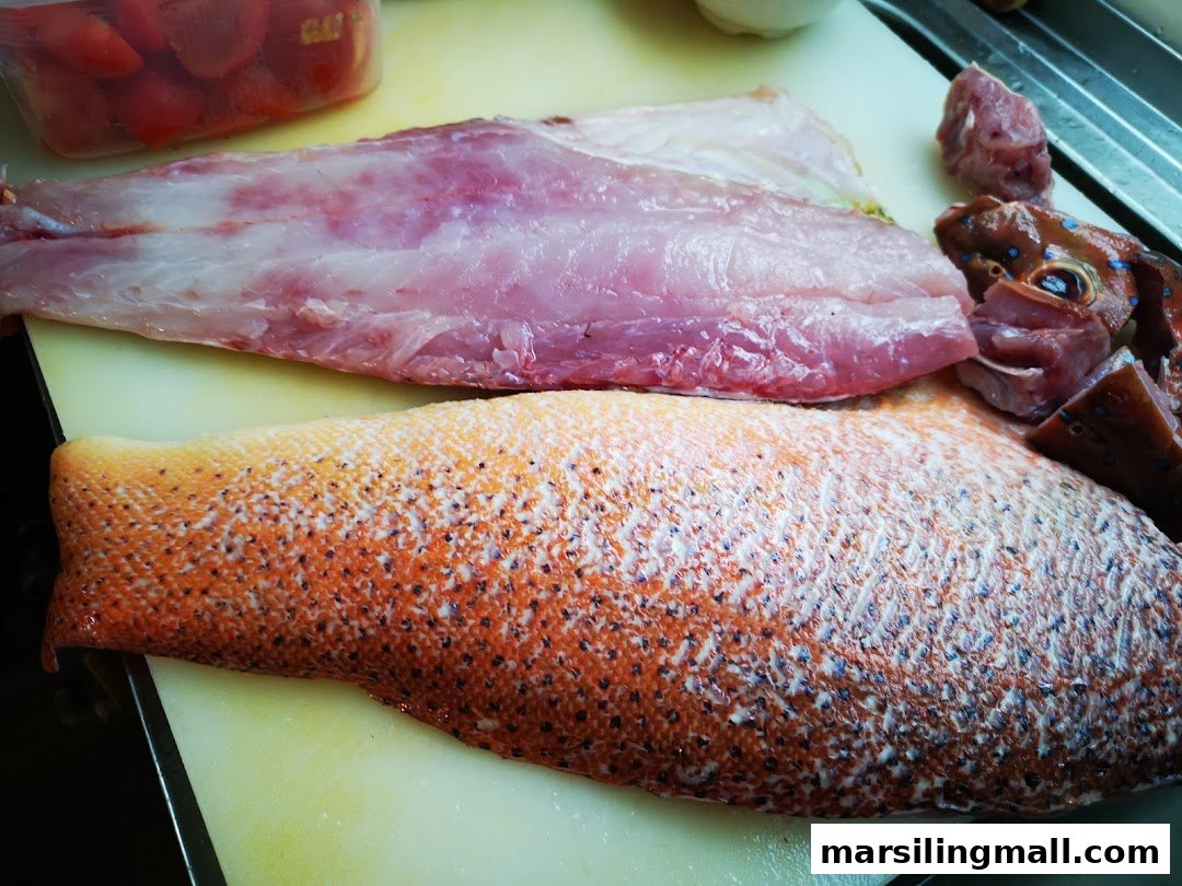 Freshly prepared raw fish fillets and whole fish on a cutting board, ready for cooking.