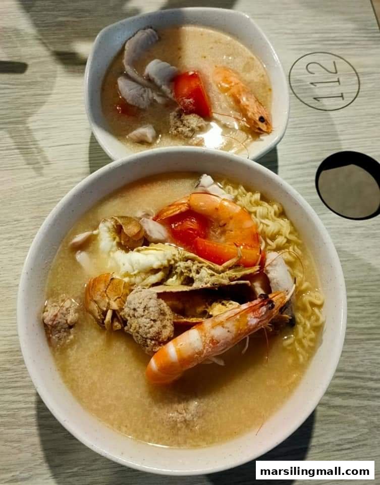Two bowls of rich seafood soup with noodles, shrimp, and meatballs on a table.