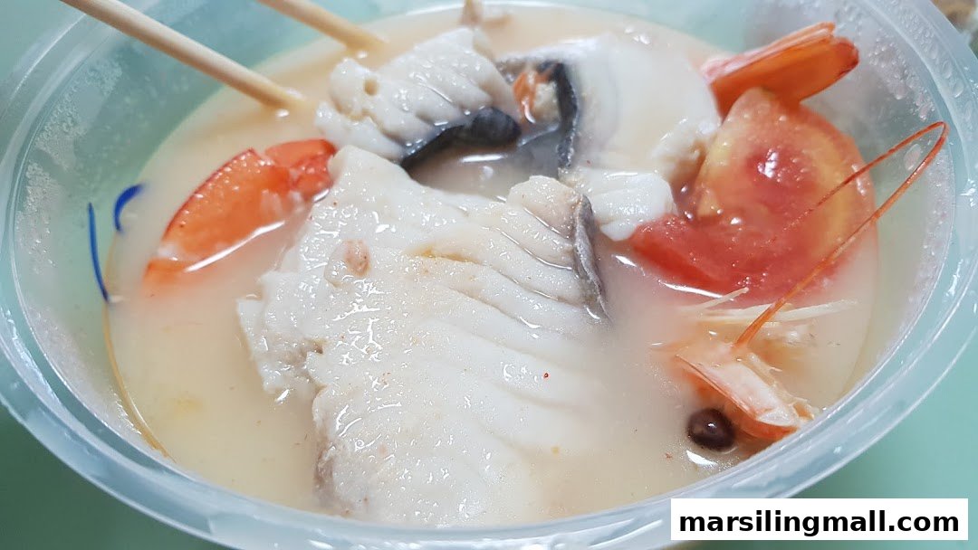 A close-up of a seafood soup with fish, shrimp, and tomatoes in a clear plastic bowl.