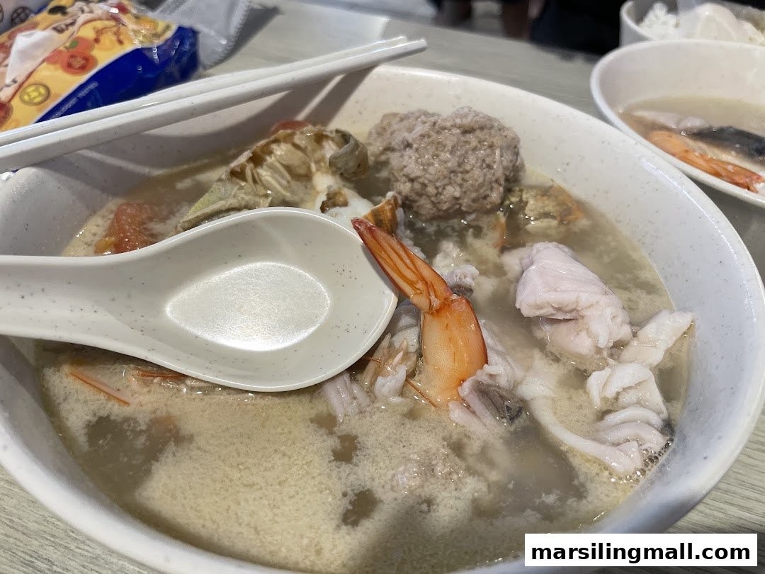 A close-up of a hearty seafood soup with shrimp, fish, crab, and a meatball.