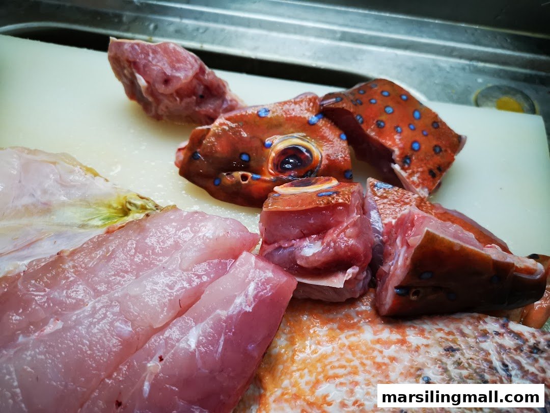 Freshly prepared raw fish, including a blue-spotted grouper, on a cutting board.