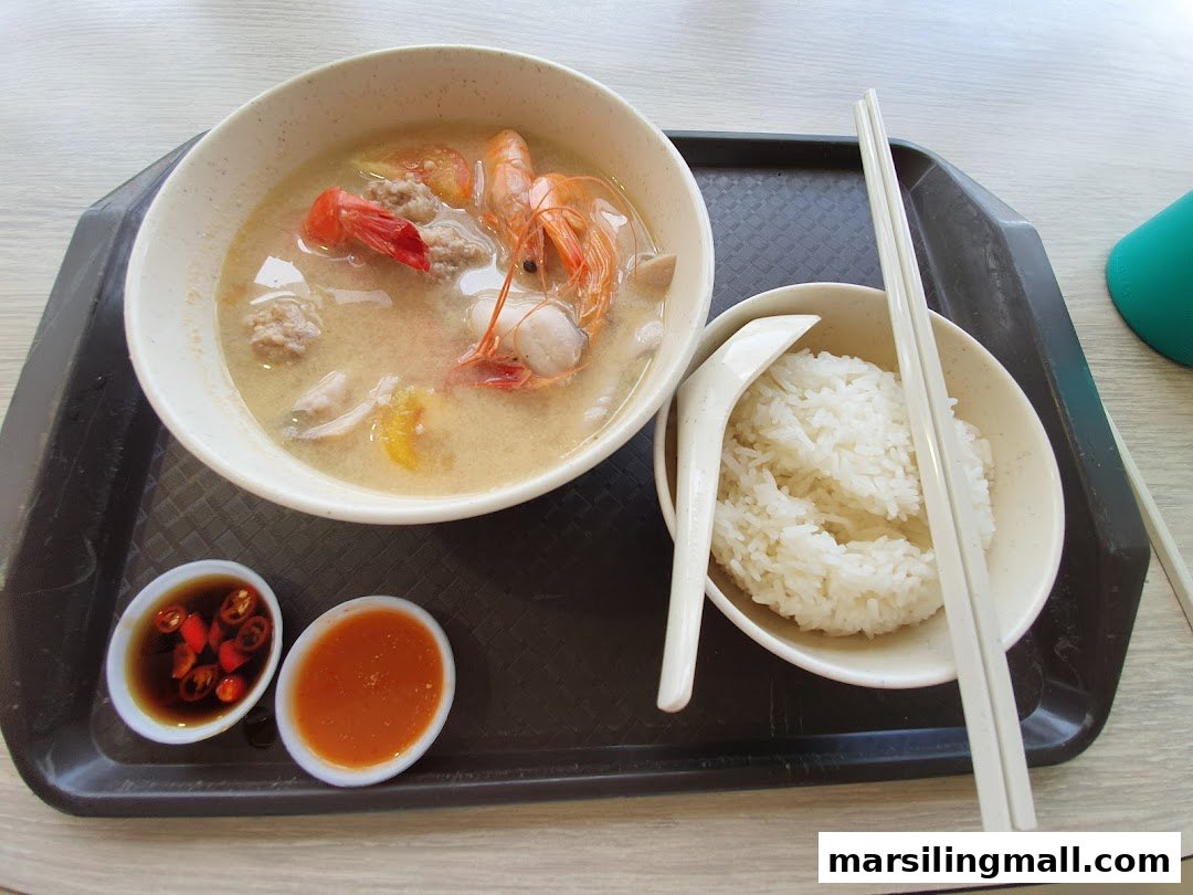 A hearty bowl of seafood soup with rice and condiments served on a tray.