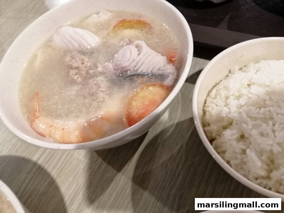 A hearty bowl of seafood soup with fish, shrimp, and minced meat, served alongside white rice.