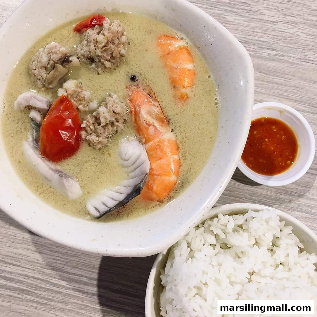 A bowl of seafood soup with fish, shrimp, meatballs, and tomatoes, served with rice and chili sauce.