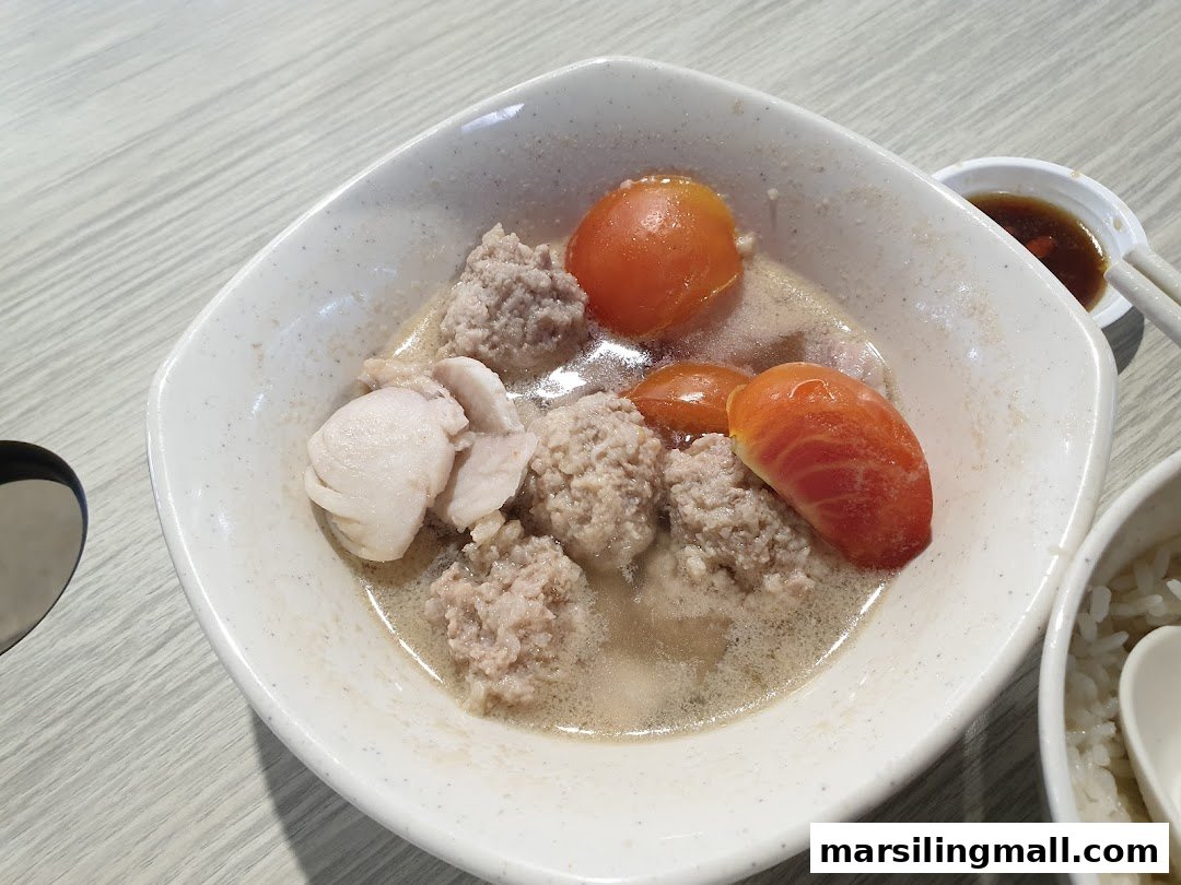 A comforting bowl of soup with meatballs, fish slices, and tomatoes.