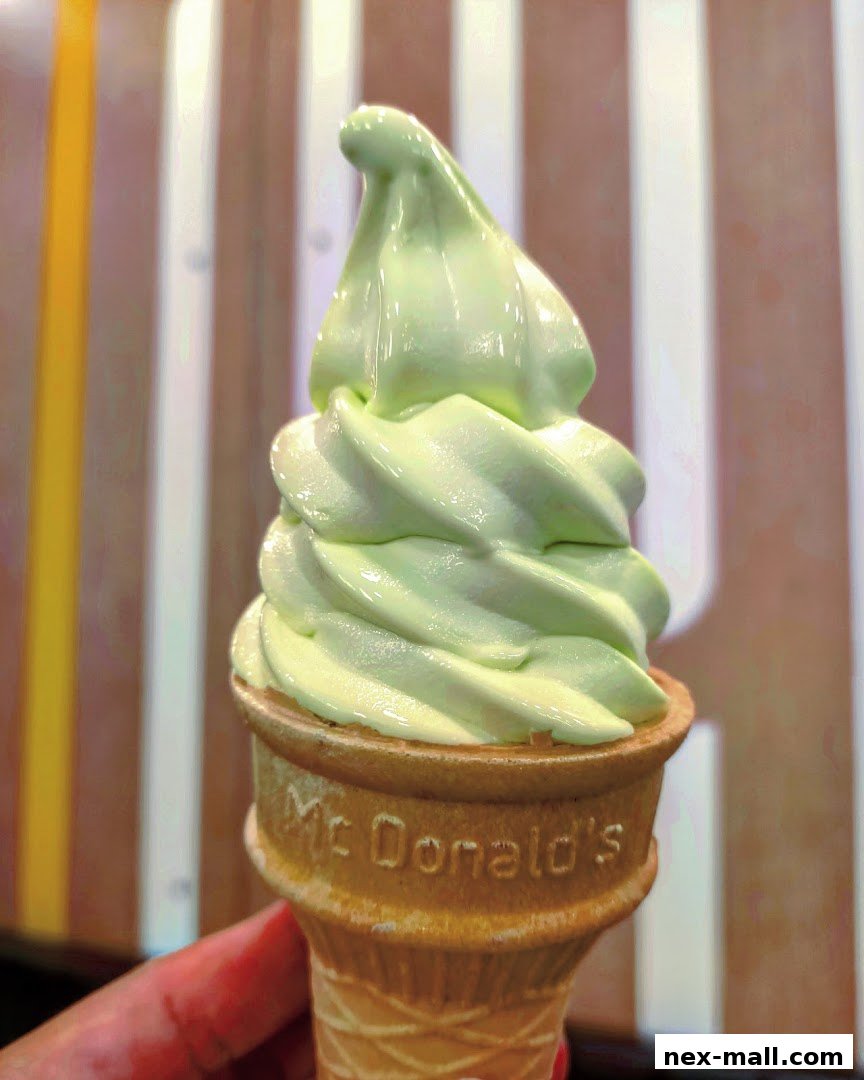 A hand holds a green soft-serve ice cream cone from McDonald's.