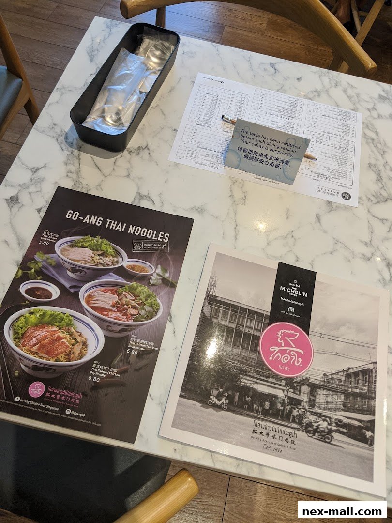 A table at Go-Ang Pratunam Chicken Rice with menus and cutlery.
