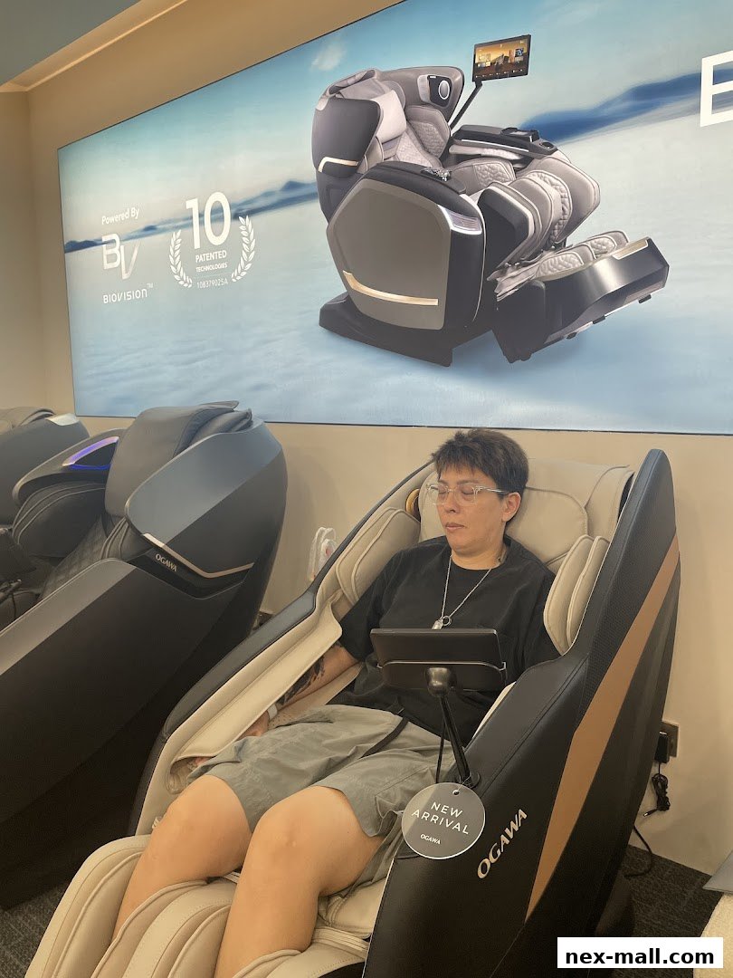 A person relaxing in an OGAWA massage chair with a large promotional display behind them.