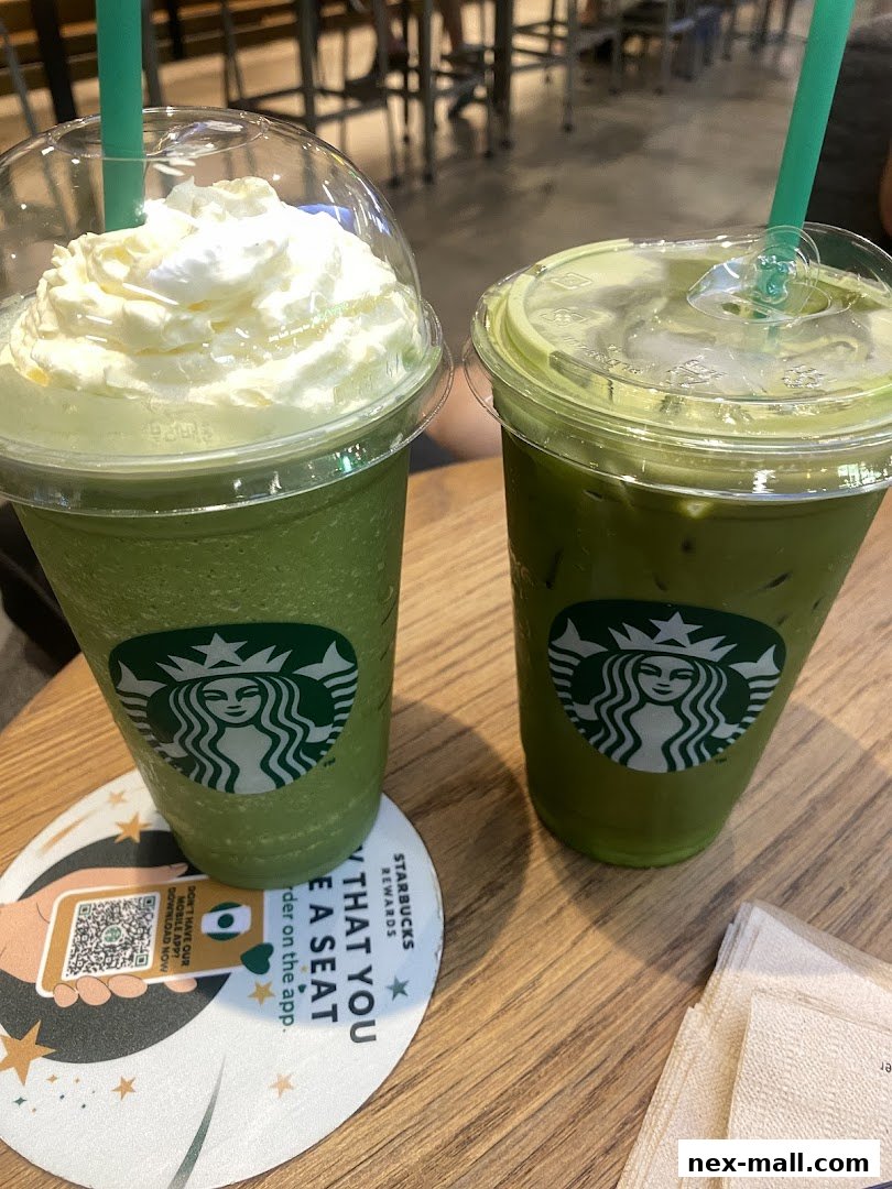 Two green Starbucks drinks, one with whipped cream, sit on a wooden table.