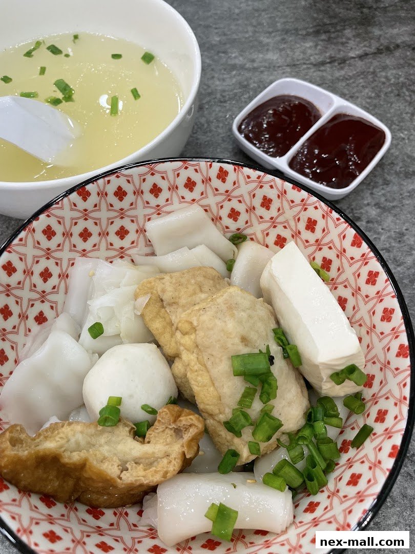 A close-up of a delicious bowl of chee cheong fun with various toppings and a side of soup.