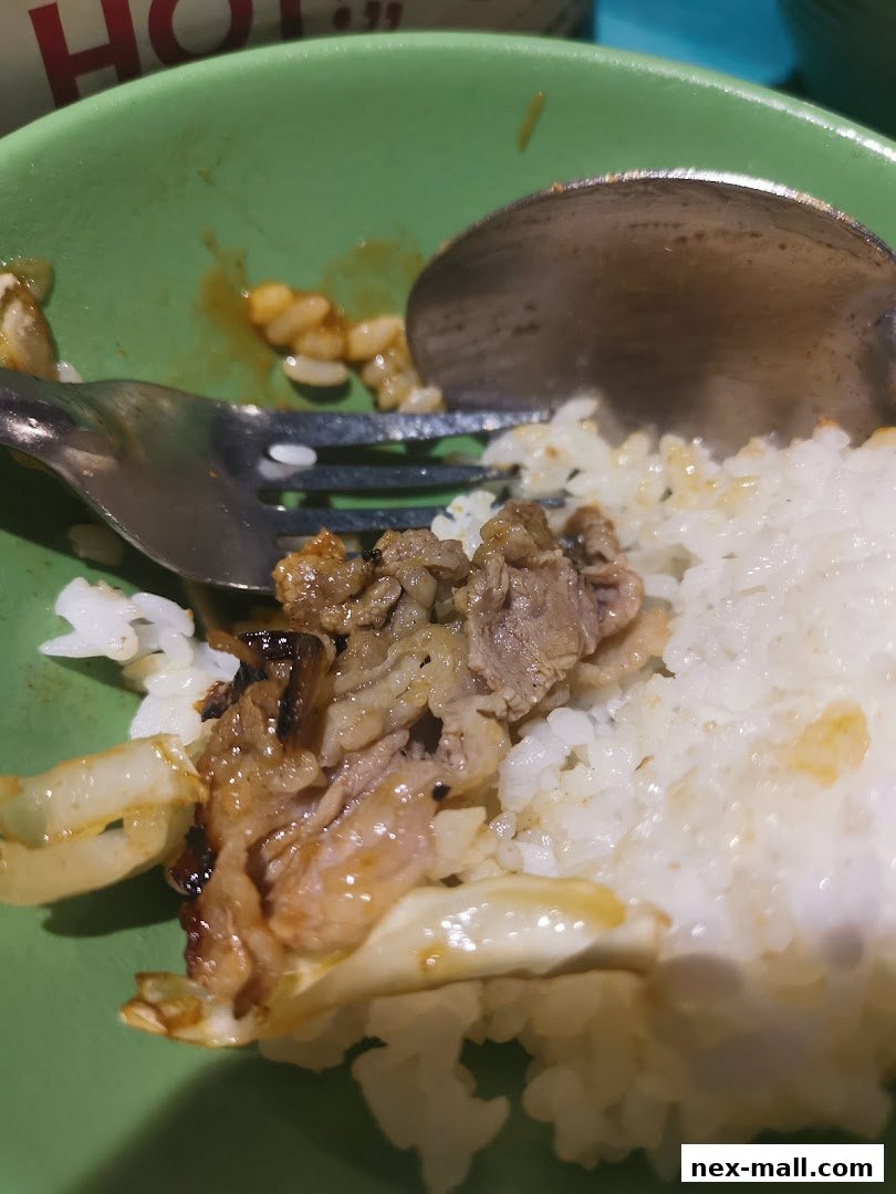 A close-up of a meal with rice, grilled meat, and onions in a green bowl.