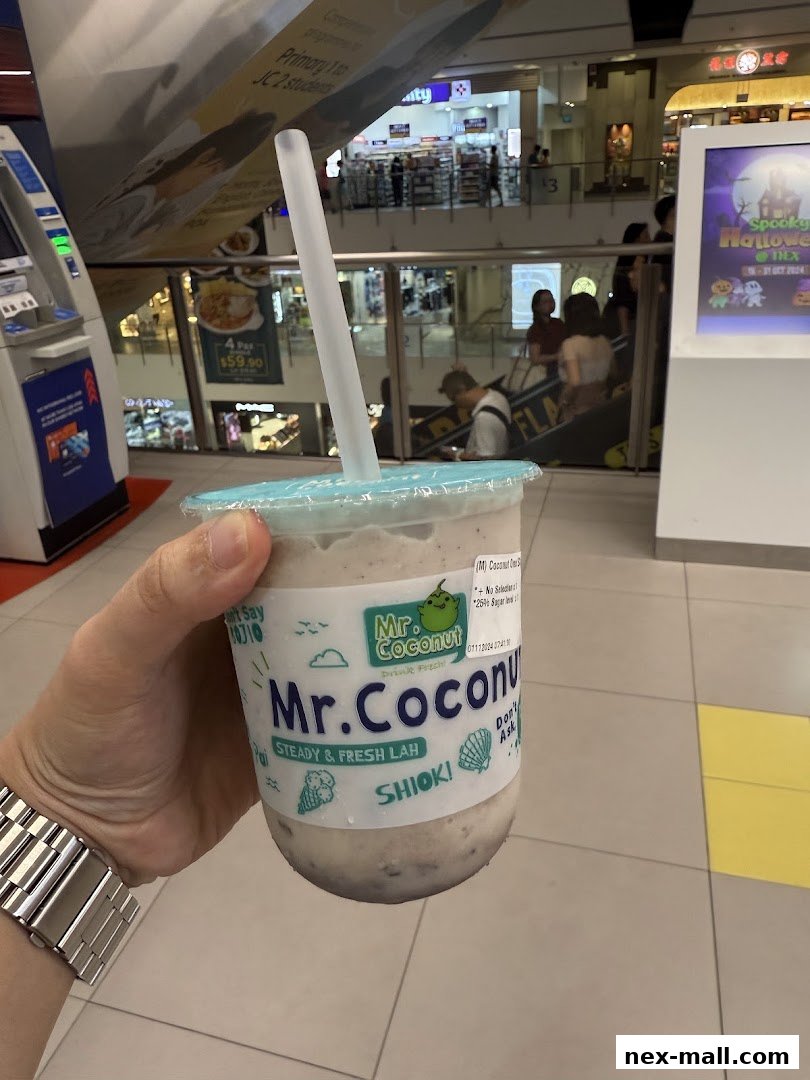 A hand holds a Mr. Coconut drink with the mall interior in the background.