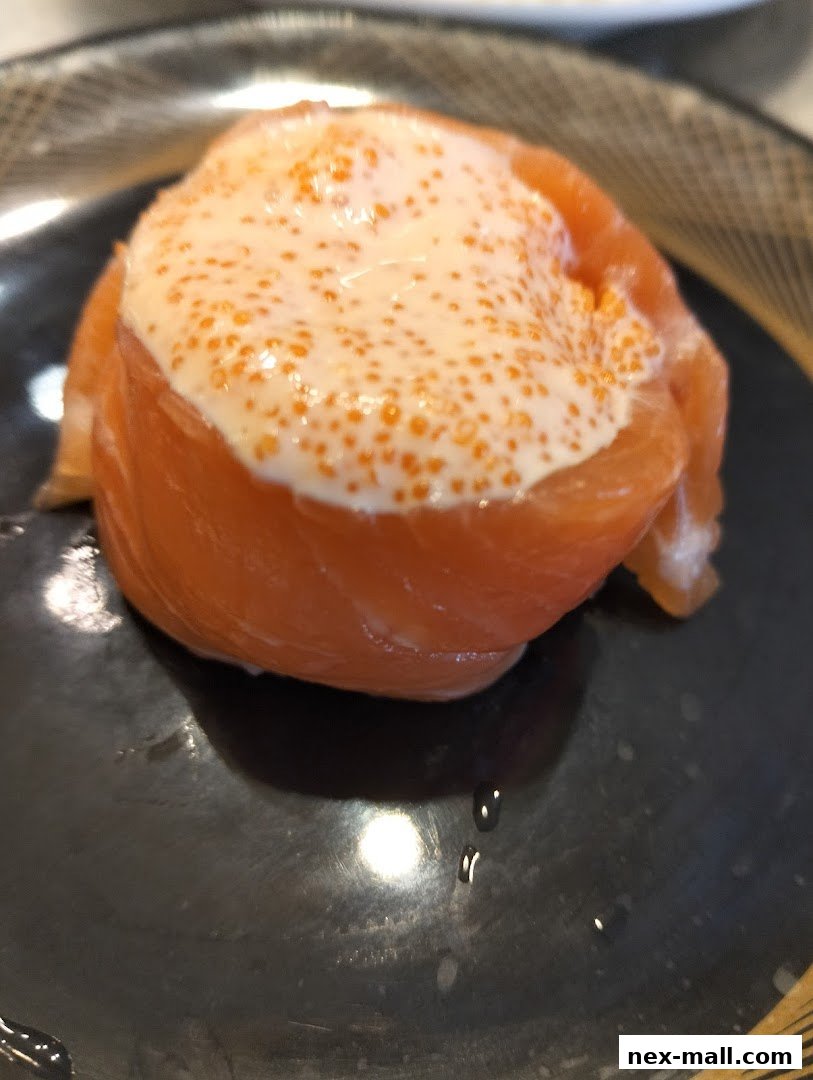 A close-up of a salmon sushi roll topped with creamy sauce and tobiko.
