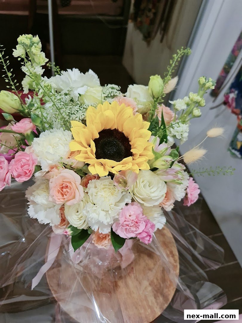 A beautiful floral arrangement featuring a sunflower, roses, and other assorted flowers.