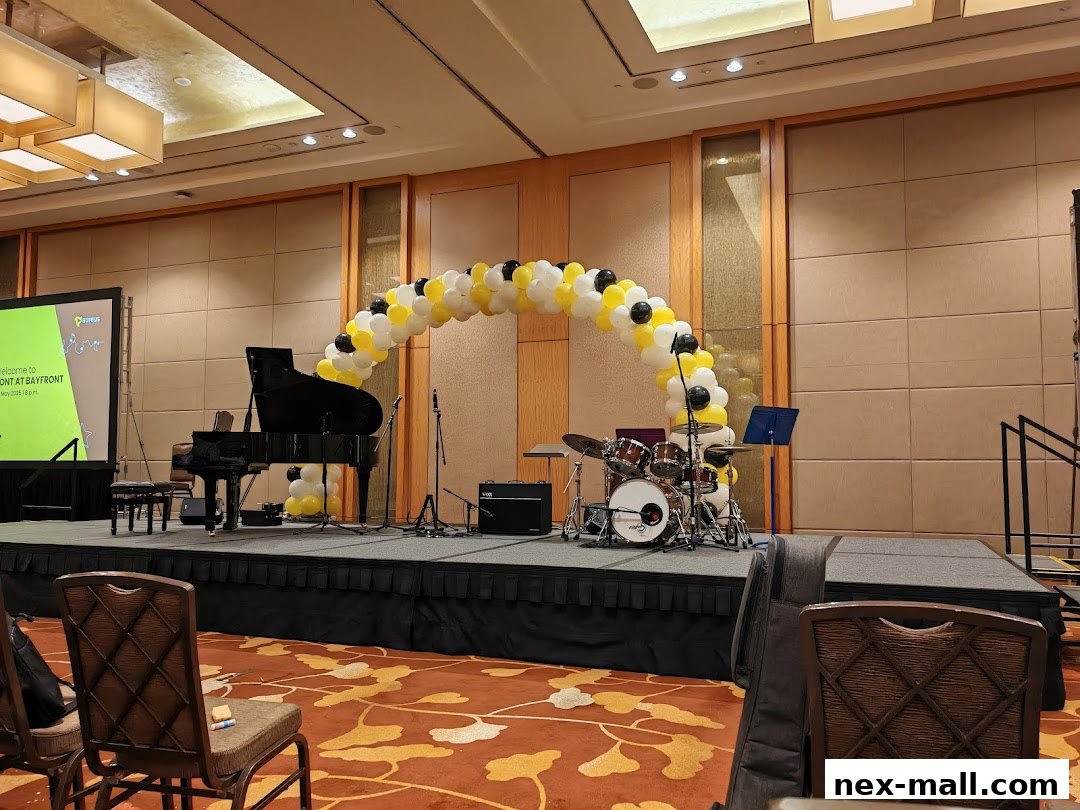 A stage set up with a grand piano, drum set, and balloon arch for a performance.