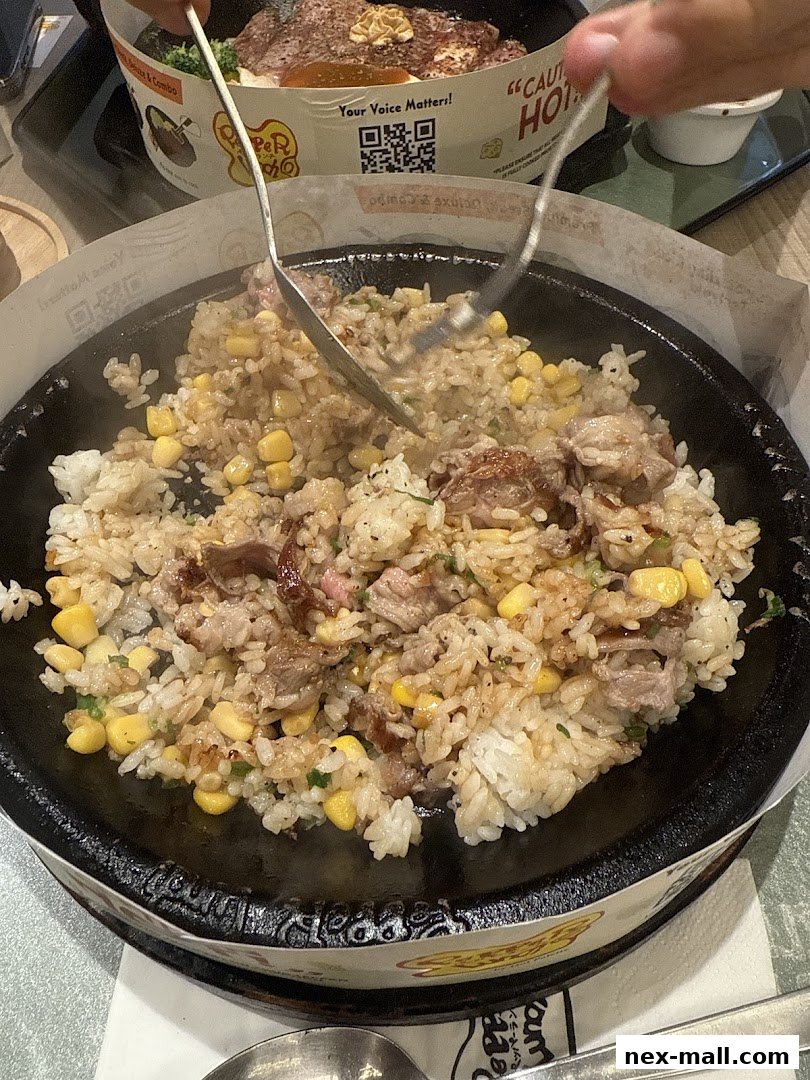 A sizzling hot plate of rice with beef and corn, being mixed with a fork and spoon.