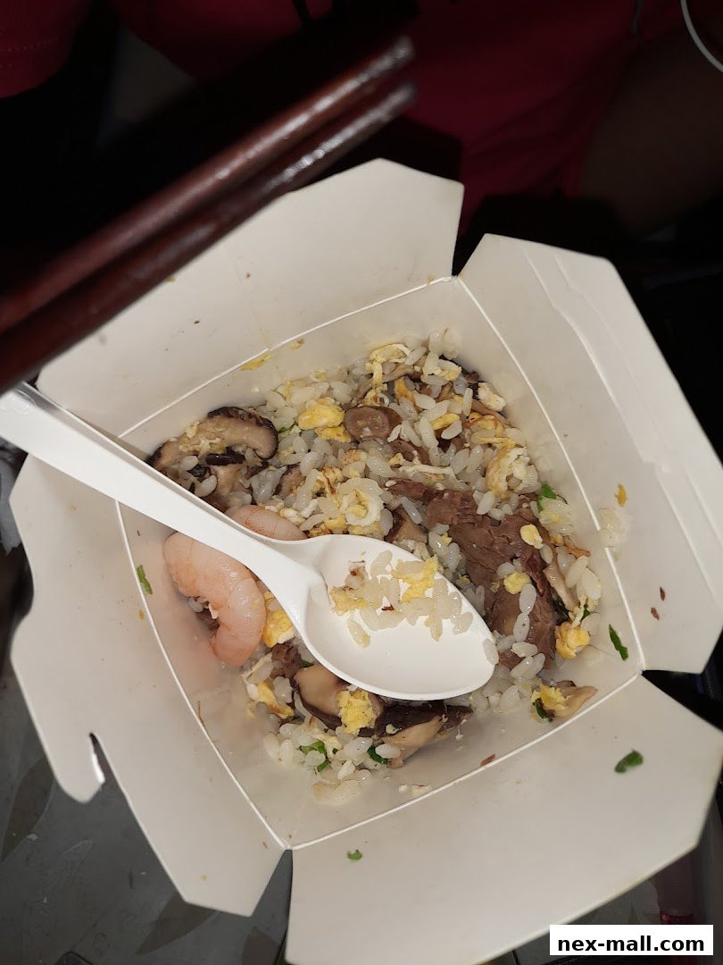 A take-out box filled with fried rice, beef, shrimp, and mushrooms, with chopsticks and a spoon.