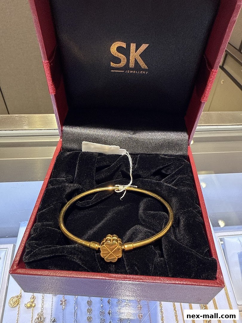 A gold bracelet with a clover charm displayed in a red jewelry box.