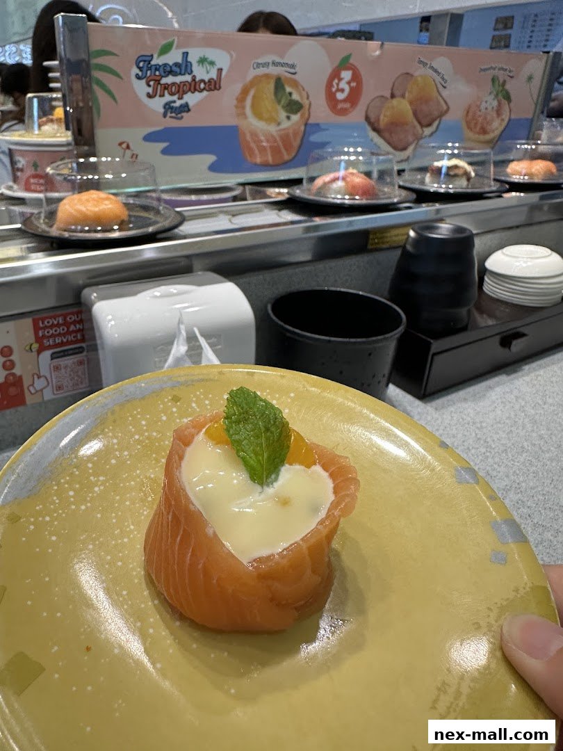 A close-up of a salmon sushi roll with creamy filling and mint on a yellow plate.