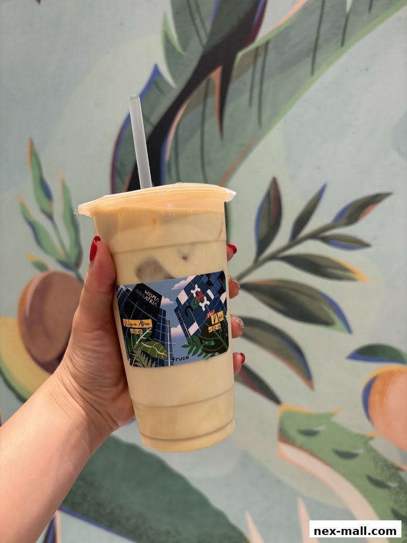 A hand holds a refreshing beverage with a tropical-themed mural in the background.