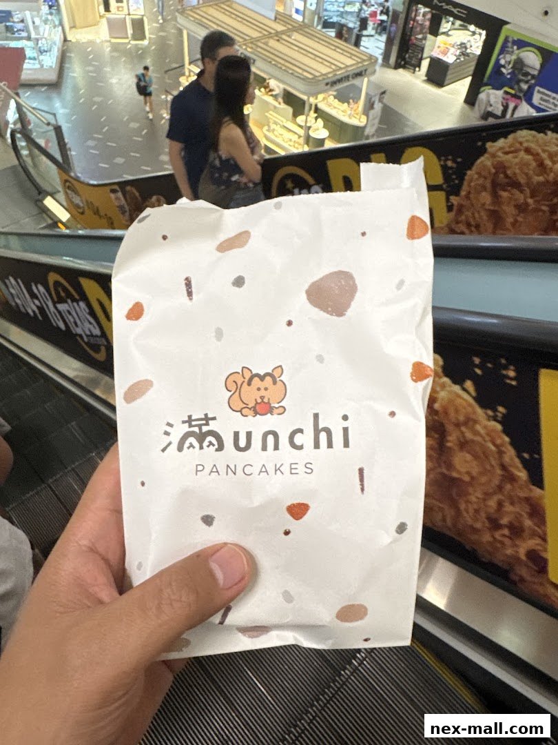 A hand holds a paper bag with the Munchi Pancakes logo, with a mall interior in the background.
