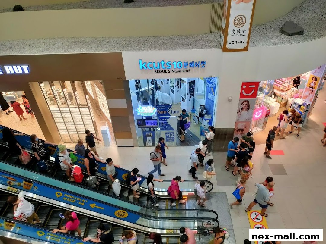 A busy shopping mall with people on escalators and in front of shops, including kcuts.
