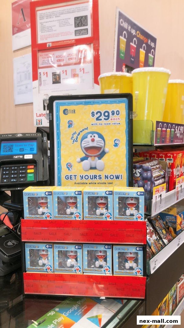 A 7-Eleven counter displaying Doraemon merchandise and payment terminals.