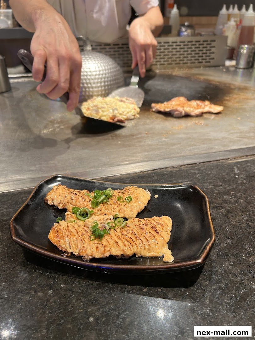 Chef preparing food on a teppanyaki grill, with a plate of grilled salmon in the foreground.