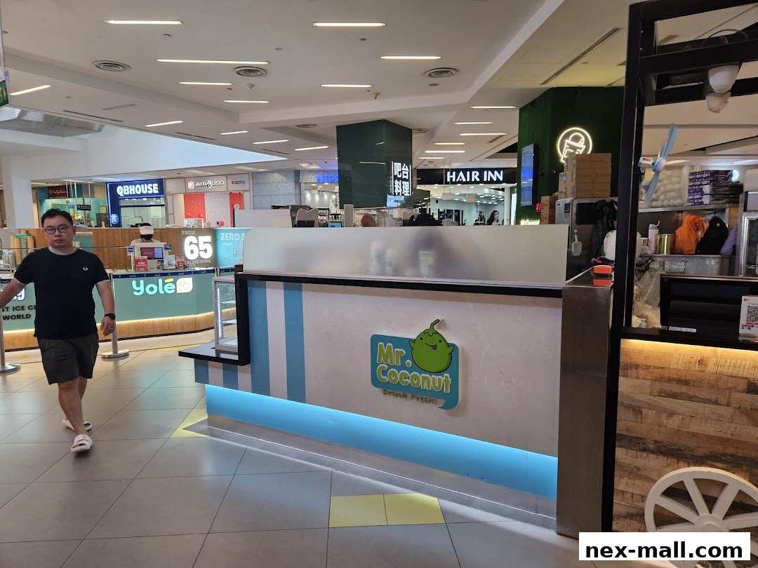 A man walks past the Mr. Coconut drink stall in a shopping mall. Other shops are visible in the background.