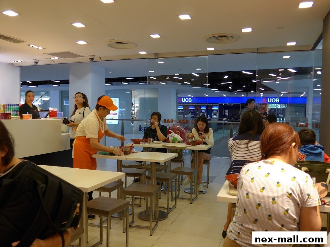 Diners are seated at tables inside a bright, modern eatery with a staff member preparing food.