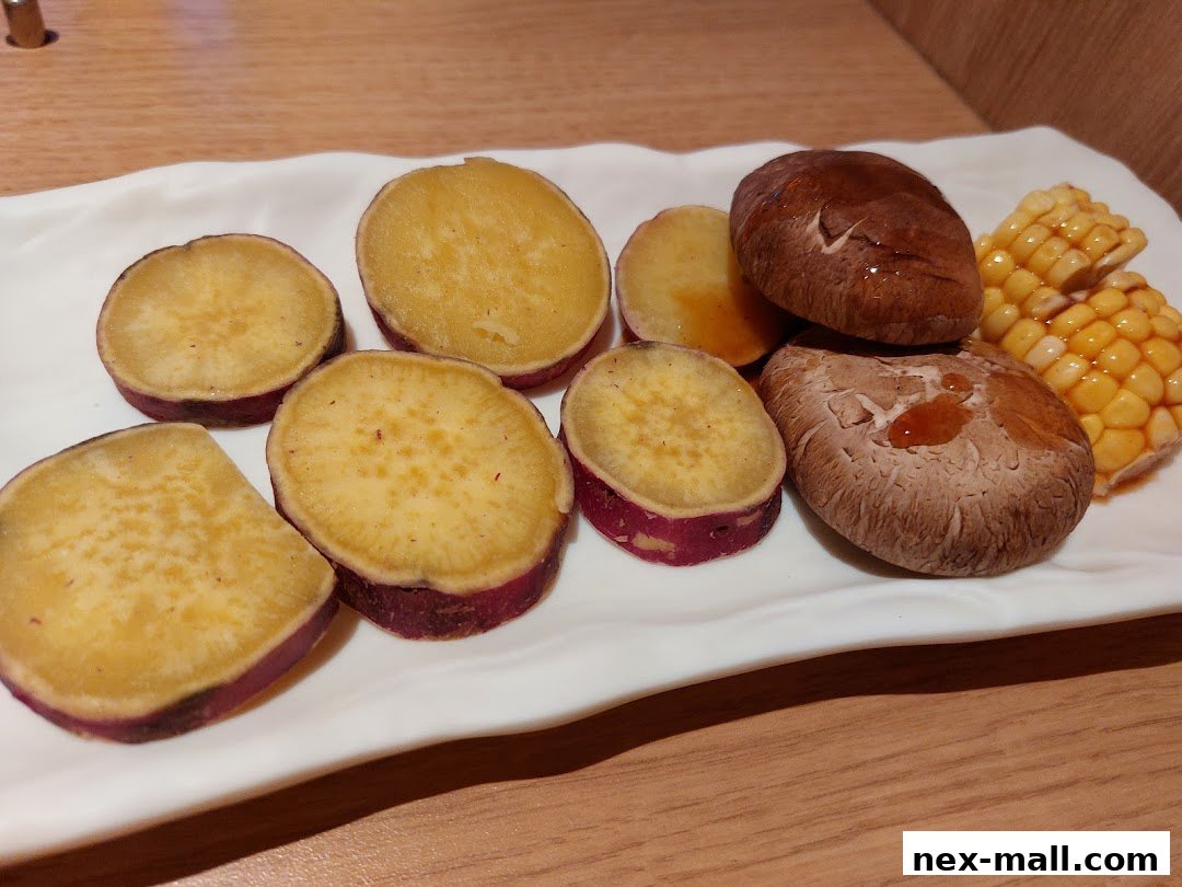 A white plate holds sliced sweet potatoes, shiitake mushrooms, and corn on the cob.