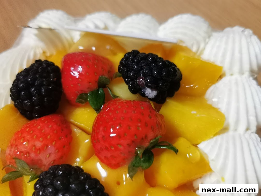 A close-up of a delicious cake topped with fresh strawberries, blackberries, and mango chunks, adorned with whipped cream.
