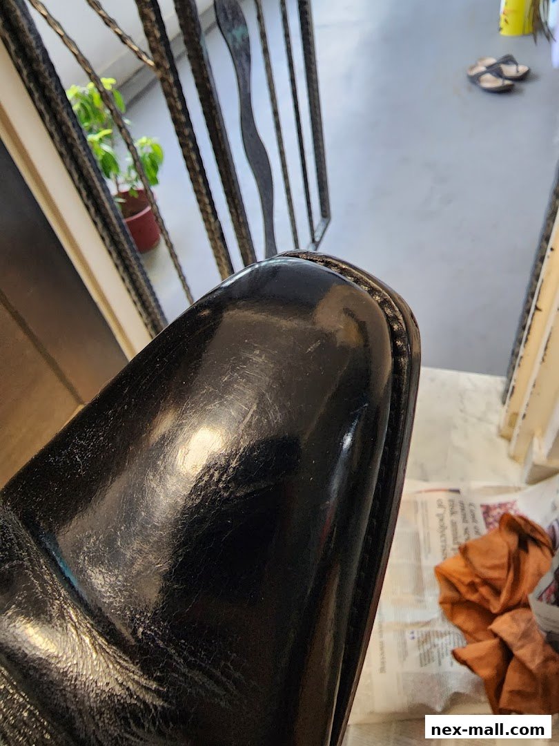 Close-up of a shiny black shoe with visible wear and tear, next to a metal railing.