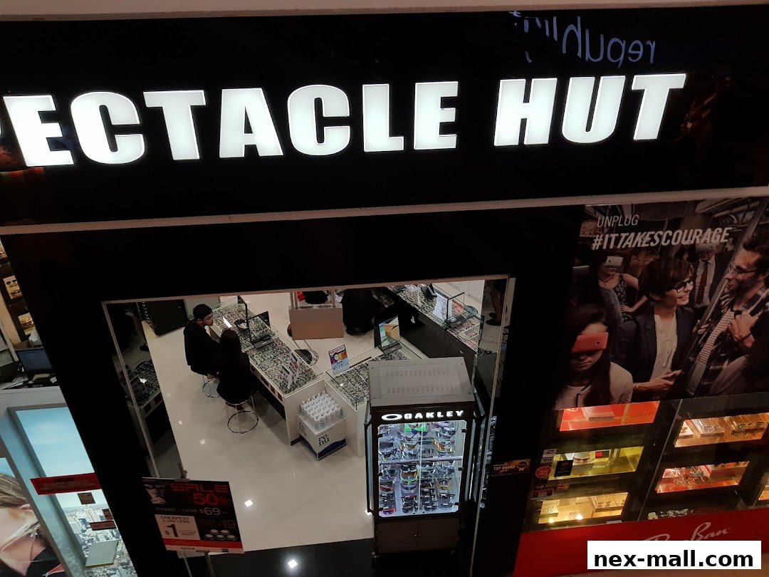 Spectacle Hut NEX shop front with illuminated signage and displays of eyewear.