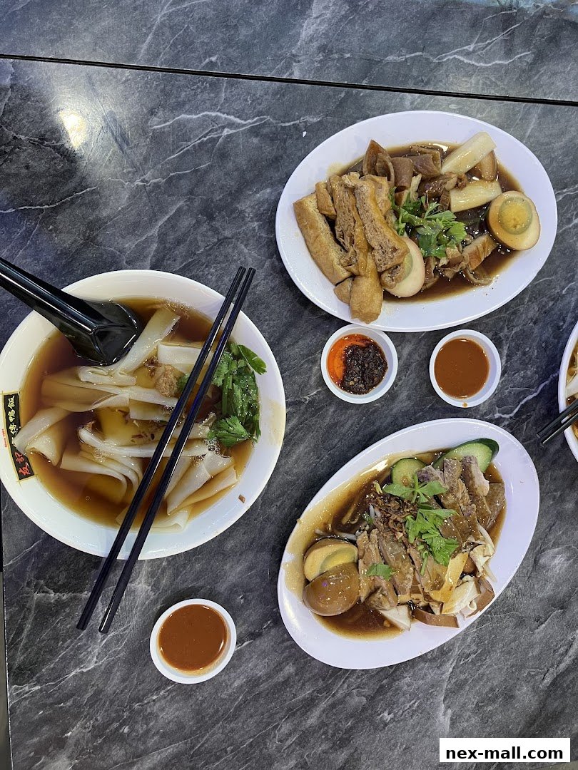 A top-down view of three plates of braised dishes and a bowl of noodles with dipping sauces.