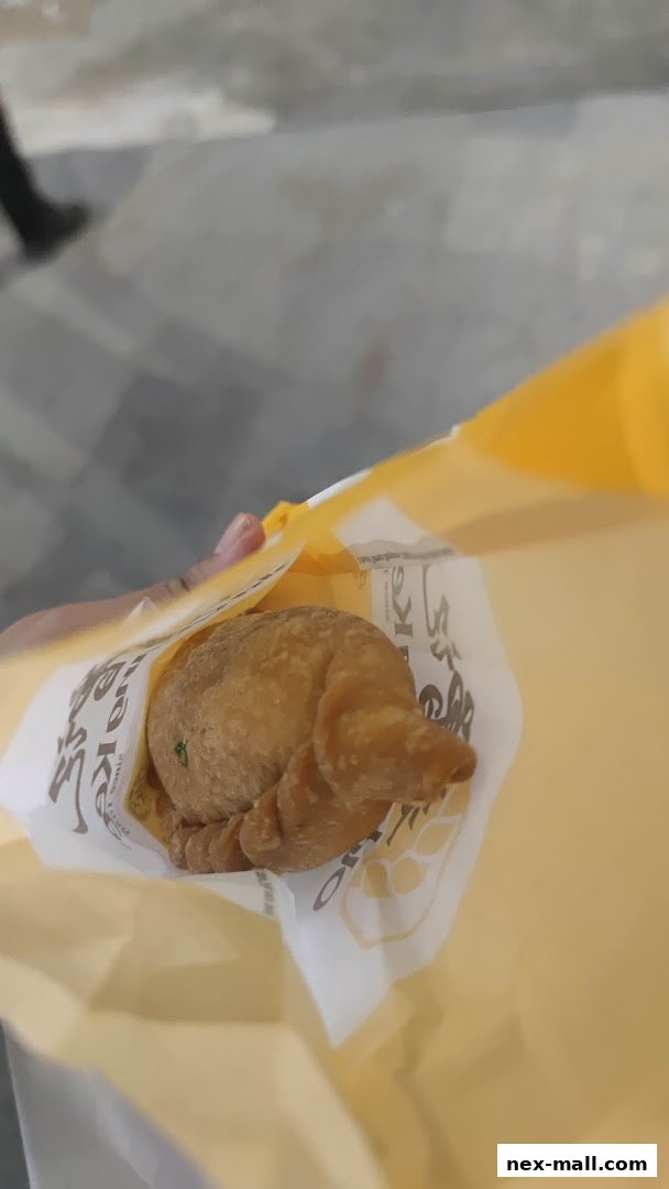 A hand holds a golden-brown pastry in a yellow Old Chang Kee paper bag.
