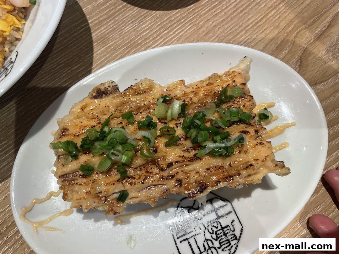 A close-up of a grilled salmon dish with mayonnaise and green onions on a white plate.