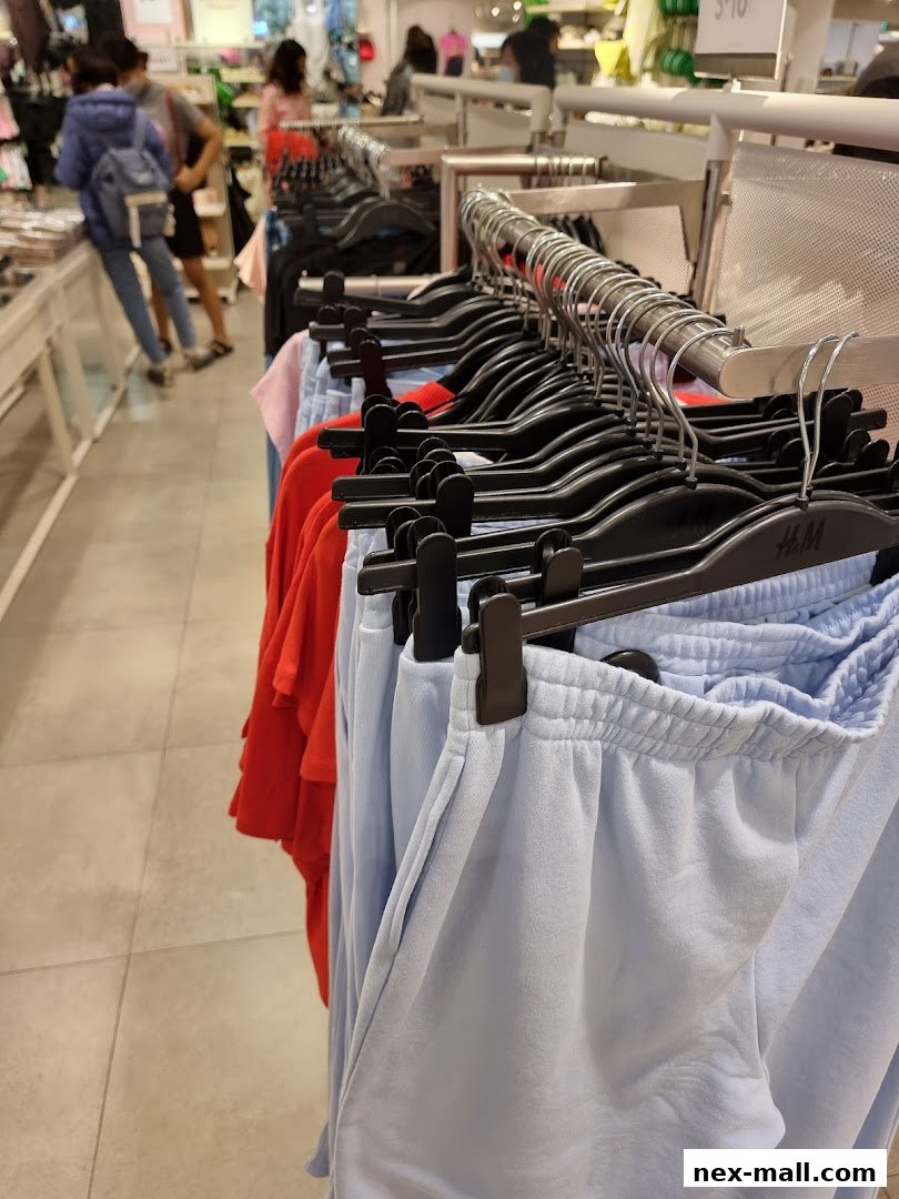 Close-up of light blue sweatpants and red t-shirts on hangers inside an H&M store.