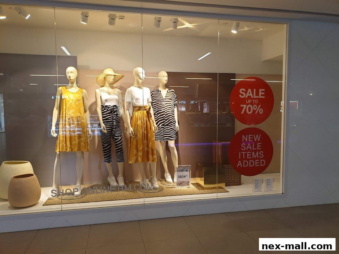 Mannequins display summer fashion in a store window with sale signs.
