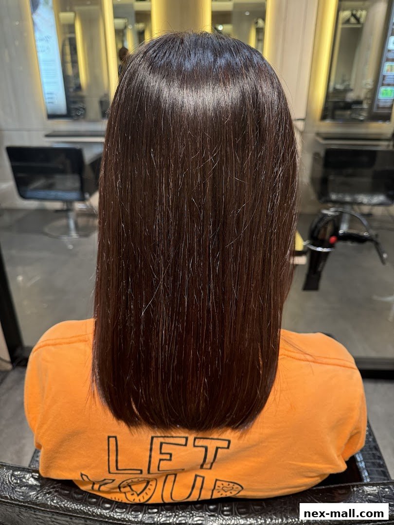 A person with long, dark, straight hair sitting in a salon chair.