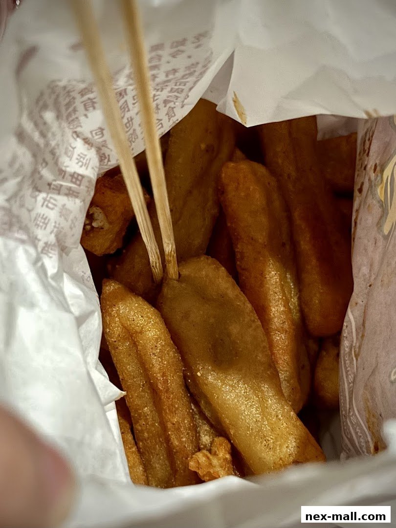 A close-up shot of crispy fried snacks on skewers inside a paper bag.