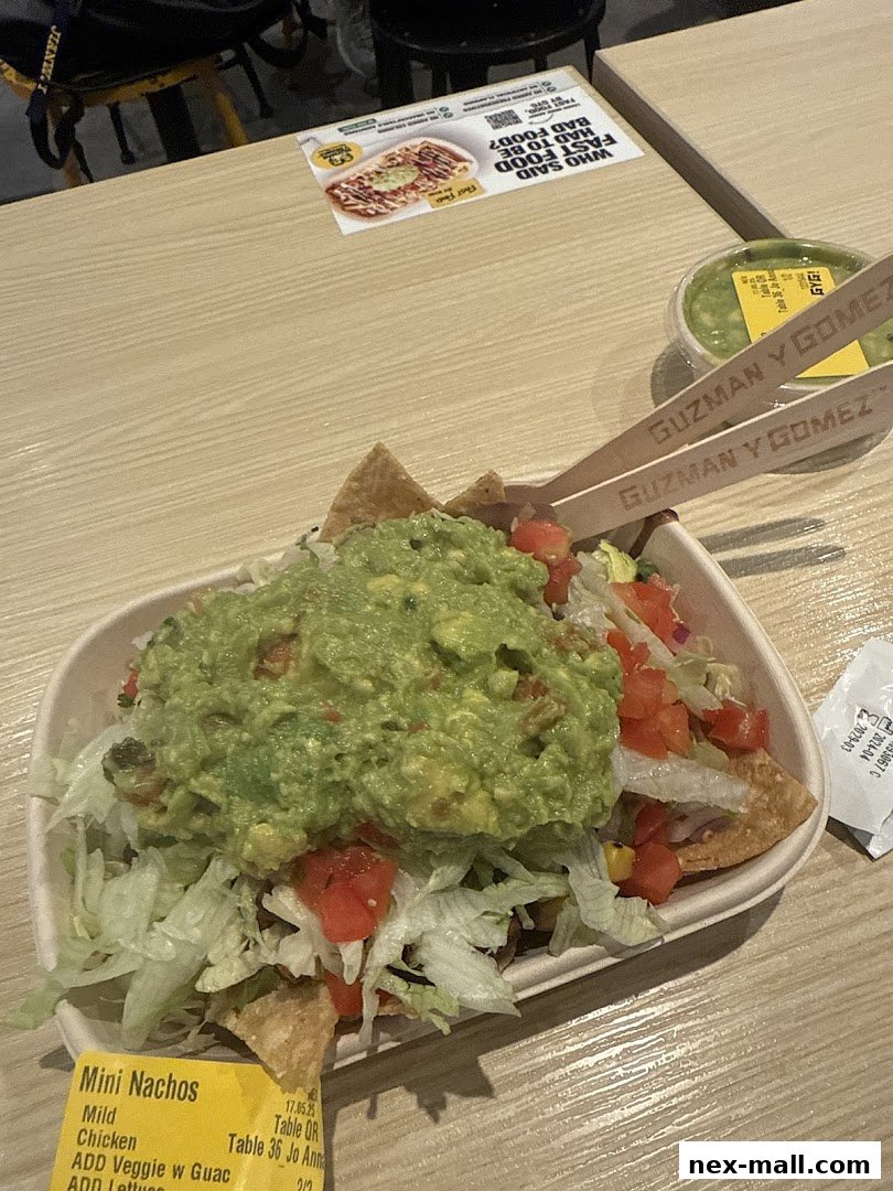 A bowl of nachos topped with guacamole, lettuce, and tomatoes, with branded cutlery.