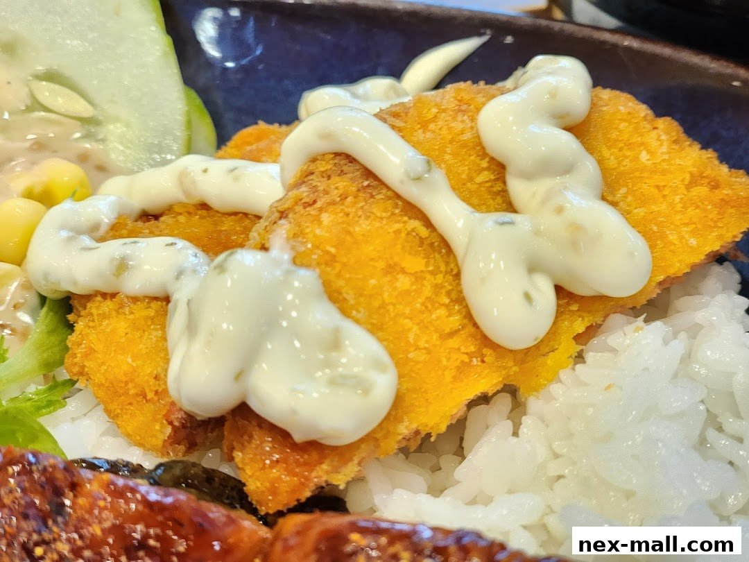 A close-up of a Yoshinoya dish featuring crispy fried fish, rice, and a creamy sauce.