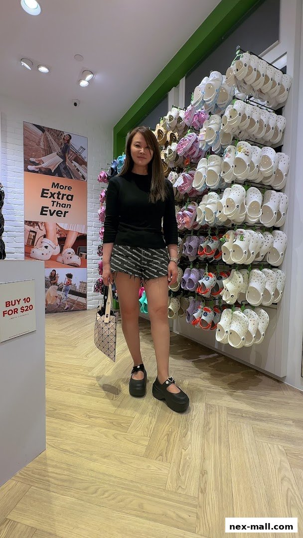 A woman stands in a Crocs store, showcasing a wall of colorful Crocs shoes.