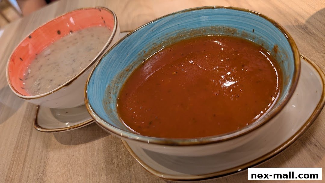 Two bowls of soup, one tomato and one creamy, are presented on a wooden table.