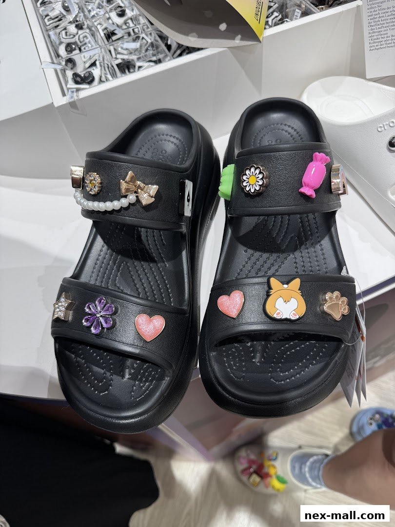 A pair of black Crocs sandals decorated with various colorful Jibbitz charms.